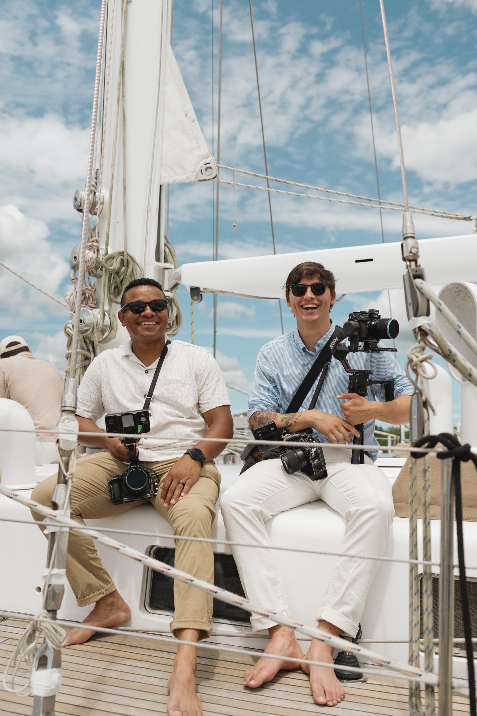 Caleb and Dom smiling on a sailboat deck, holding their cinema cameras
